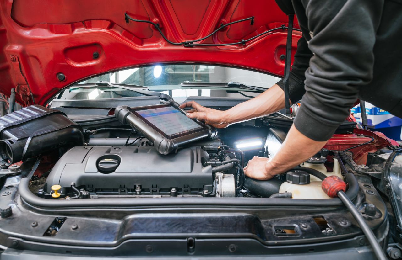 車のボンネット内で専用の診断機を操作し、点検を行う整備士